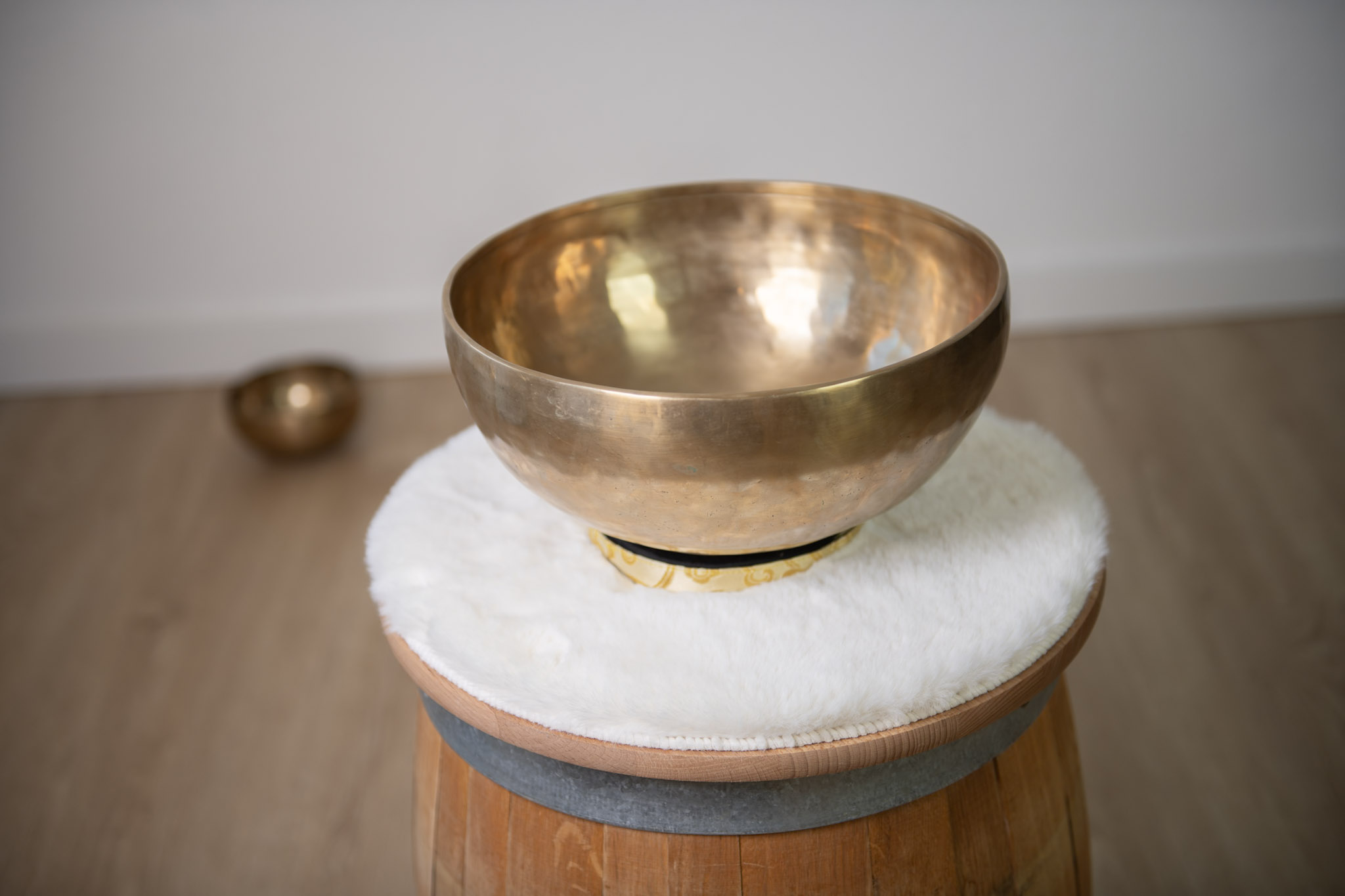 Große goldene Klangschale auf weichem Fellkissen, platziert auf einem Holzfass – beruhigende Klänge für Entspannung, Meditation und Musiktherapie.
