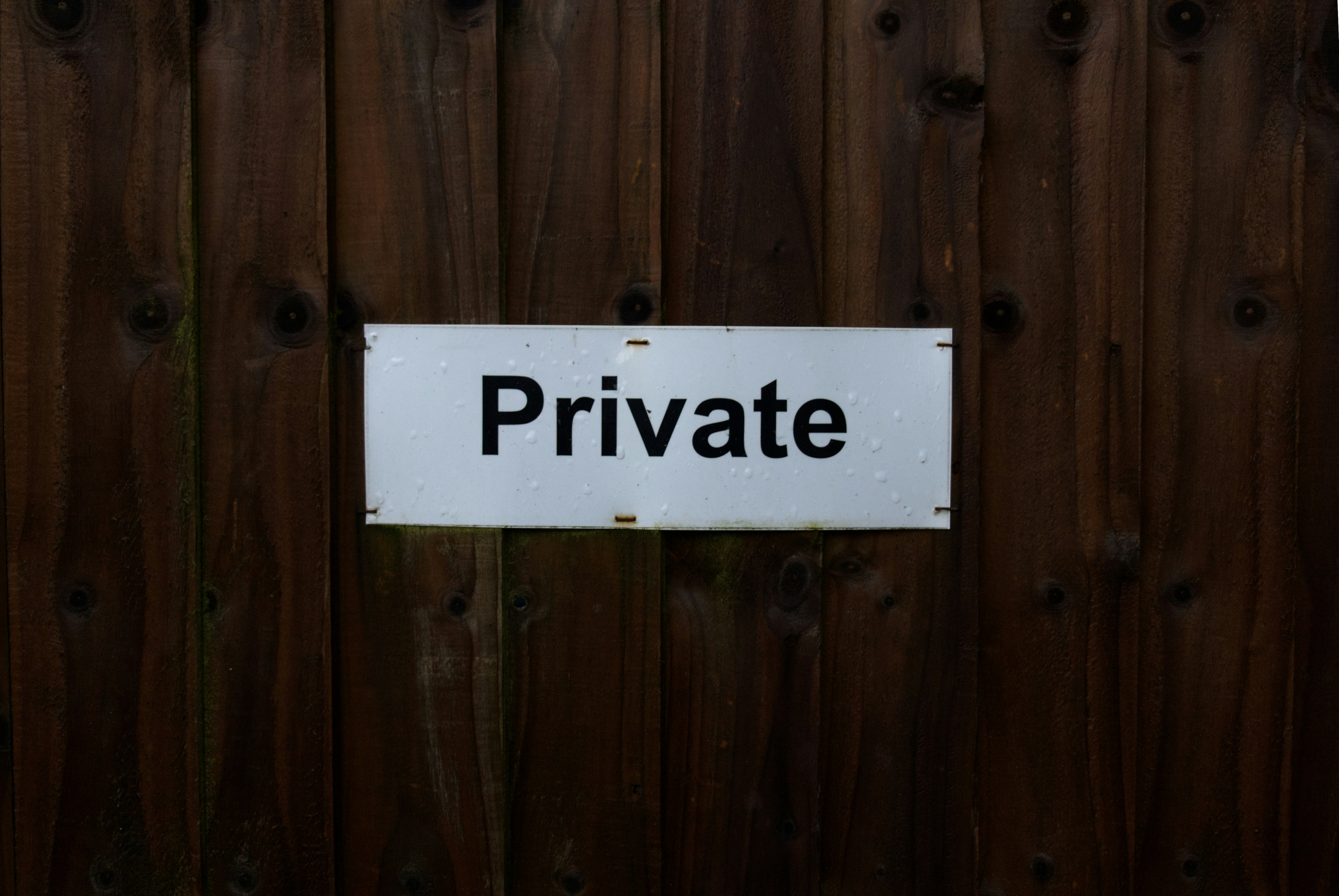 Weißes Schild mit der Aufschrift 'Private' an einer dunklen Holzwand – Symbol für Datenschutz und Privatsphäre