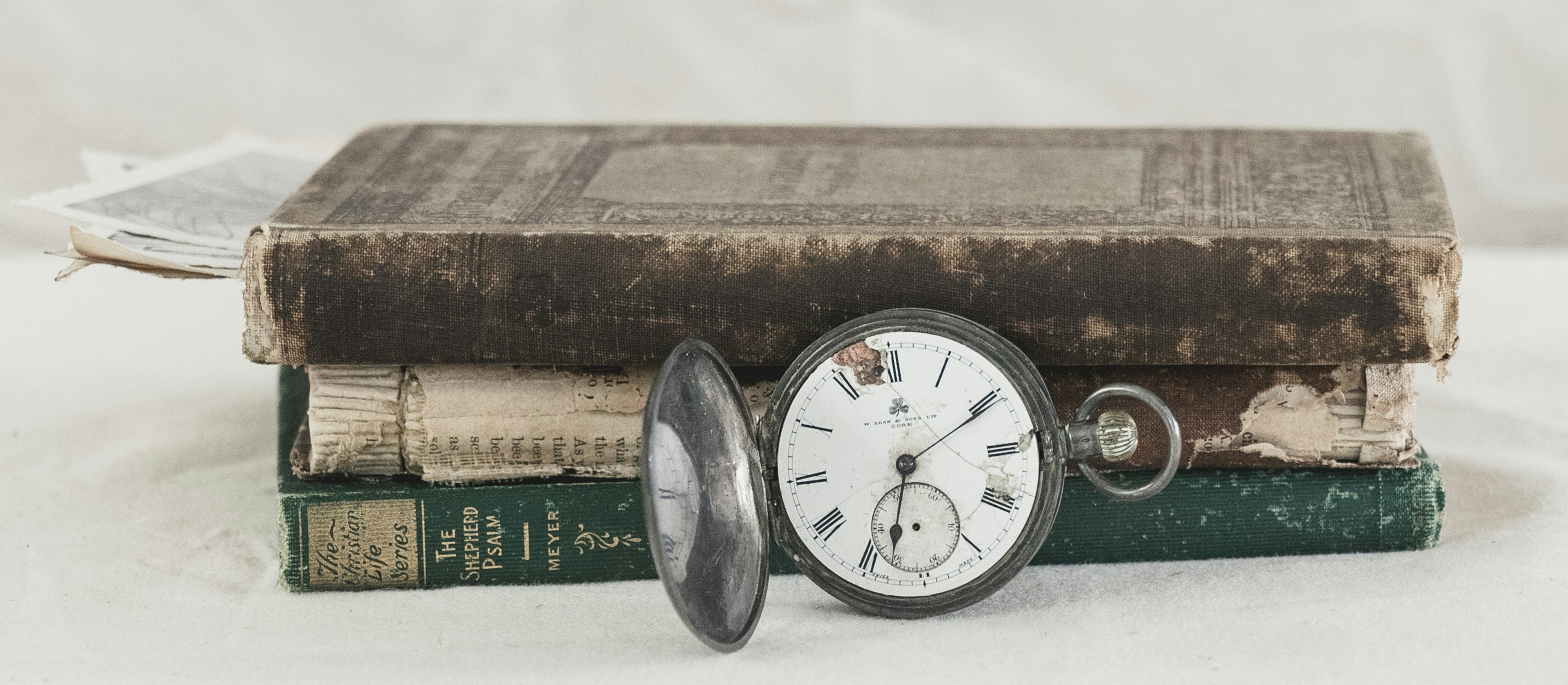 Antike Taschenuhr mit rissigem Zifferblatt liegt auf einem Stapel alter, abgenutzter Bücher – Symbol für Geschichte, Zeit und Vergänglichkeit.